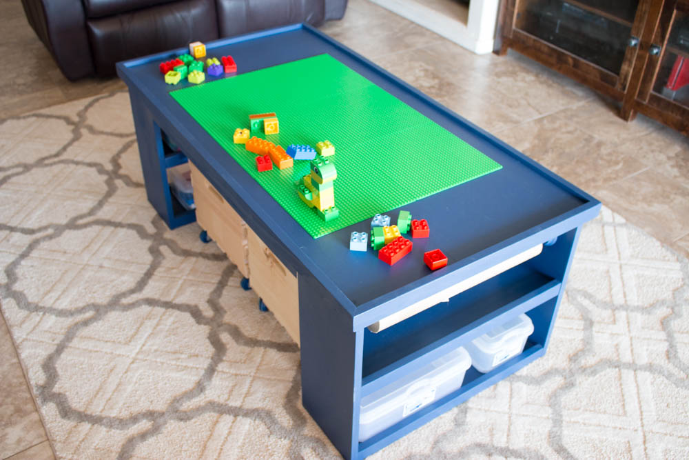 Navy blue DIY kids activity table with six green Lego base plates on top and plastic storage bins on the shelves below