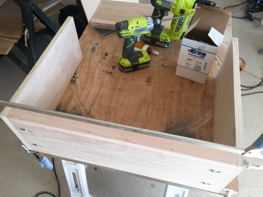 Top-down view of the DIY kids activity table base being assembled with two RYOBI drills and a box of Kreg pocket hole screws on a workbench