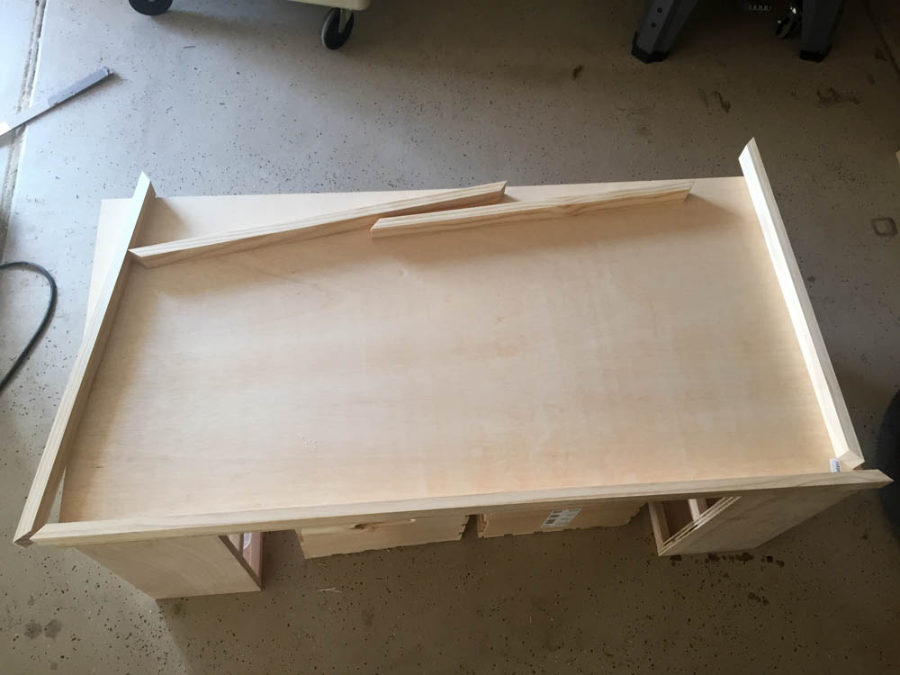 Overhead view of the unfinished DIY kids activity table tabletop with 1x2 trim pieces attached around the perimeter on a garage floor