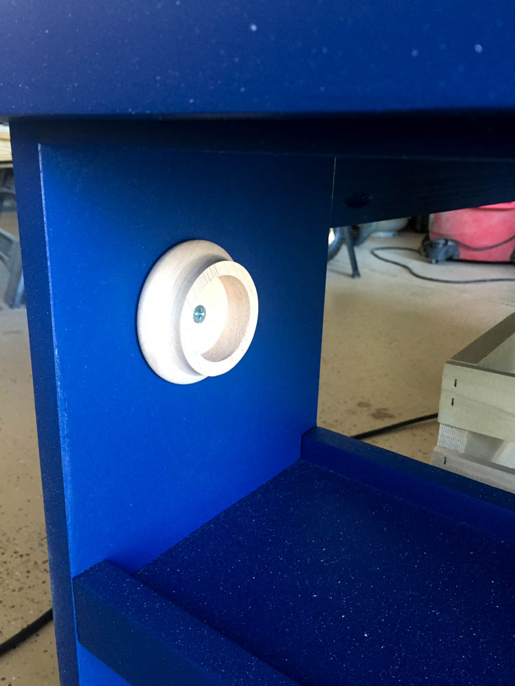 Close-up of a white closet rod socket mounted on the navy blue painted side of a DIY kids activity table used to hold the drawing paper roll dowel