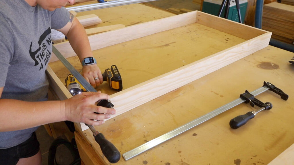 Assembling the 1x4 pine cornhole board frame with clamps and pocket screws on a workbench