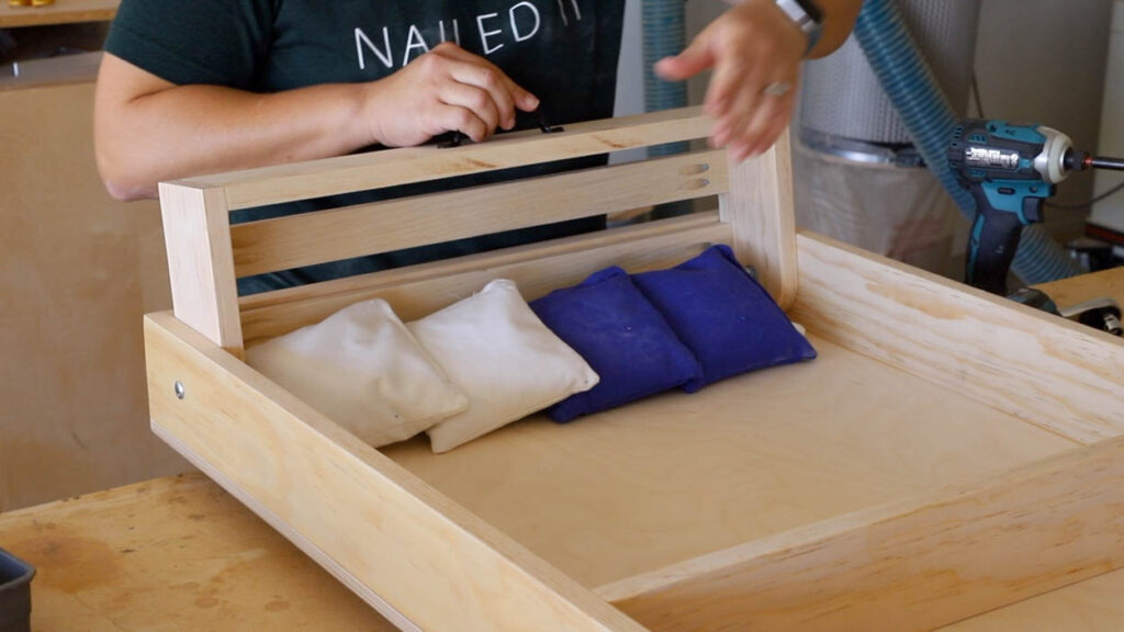 Drilling in a handle on top of the cornhole board bean bag holder for easy opening