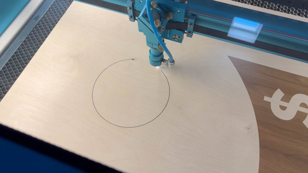 Thunder Laser cutter tracing the circle cut for the cornhole hole on a laser-engraved plywood board