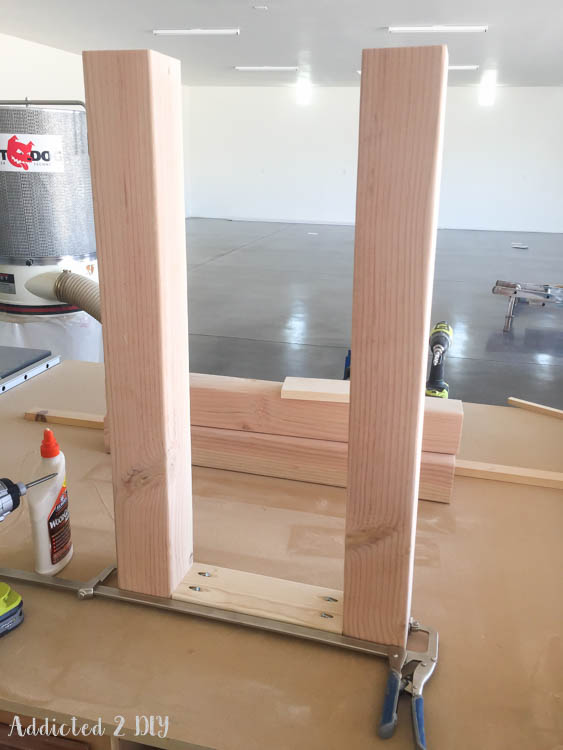 Two 4x4 legs connected by a 1x4 top support being assembled with pocket screws and wood glue on a workbench with clamps