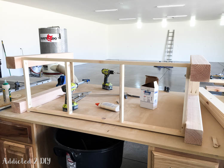 Bottom shelf support frame assembled with 1x2 boards and pocket screws, attached between two leg assemblies on a workshop table