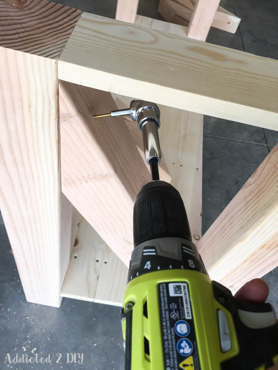 Ryobi drill with offset adapter drilling a pilot hole into the X-brace end where it meets the 4x4 leg of the DIY outdoor console table