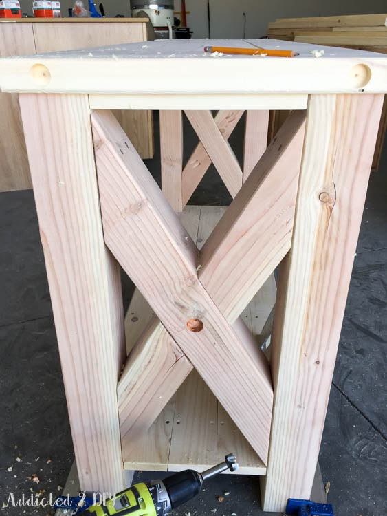 Fully assembled unfinished DIY rustic outdoor console table showing the X-brace detail, breadboard ends with countersunk bolt holes, and completed lower shelf