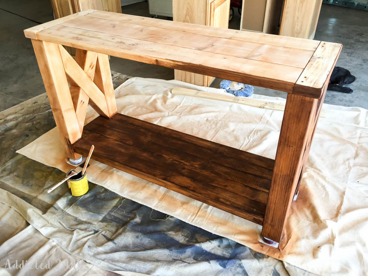 DIY rustic outdoor console table mid-gel-stain application showing the rich hickory brown color from Minwax gel stain covering the previously sanded orange base