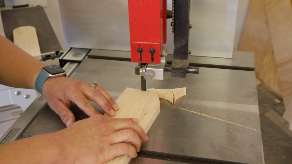 Cutting the curved radius on the top of a cornhole board leg on a red bandsaw