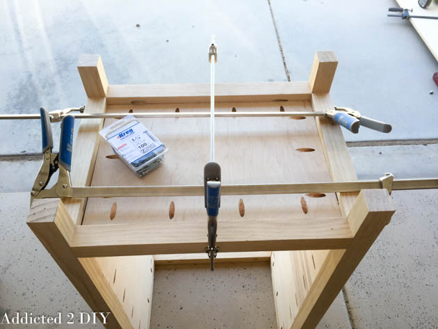 Top-down view of wine cabinet frame with bottom shelf clamped in place and a box of Kreg 1-1/4 inch pocket screws sitting on the shelf