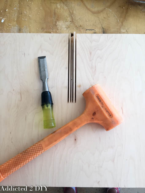 3/4-inch chisel and rubber mallet next to a plywood board with miter saw relief cuts made for the X wine rack notch