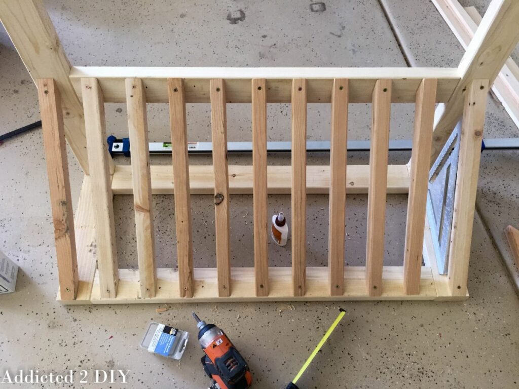Top-down view of evenly spaced 2x2 wood uprights attached to the base frame of a DIY bike rack, with a drill and tape measure nearby