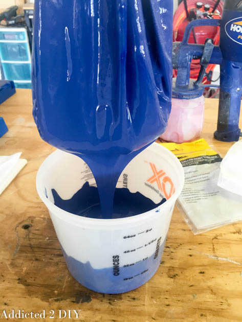 Blue latex paint being poured through a paint strainer into a mixing bucket before use in an HVLP paint sprayer