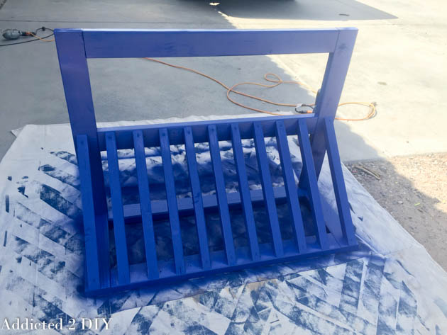 DIY wooden bike rack after the first coat of bright blue spray paint, showing good coverage on all slats and frame pieces