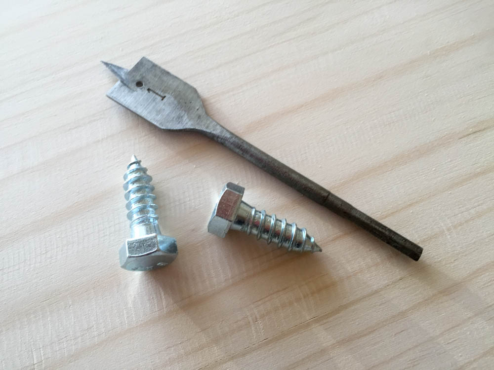 1-inch spade paddle drill bit alongside two hex-head lag bolts used for decorative leg hardware on DIY rustic nightstand