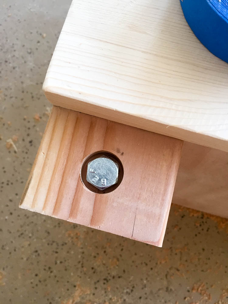 Close-up of hex-head lag bolt recessed into a 1-inch countersink hole drilled into the 4x4 wooden leg of a DIY nightstand