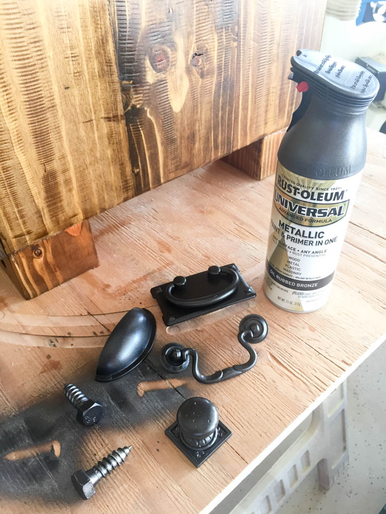 Assortment of cabinet knobs, bin pull, and bail pull hardware painted with Rustoleum Universal Metallic Oil Rubbed Bronze spray paint beside the stained nightstand leg