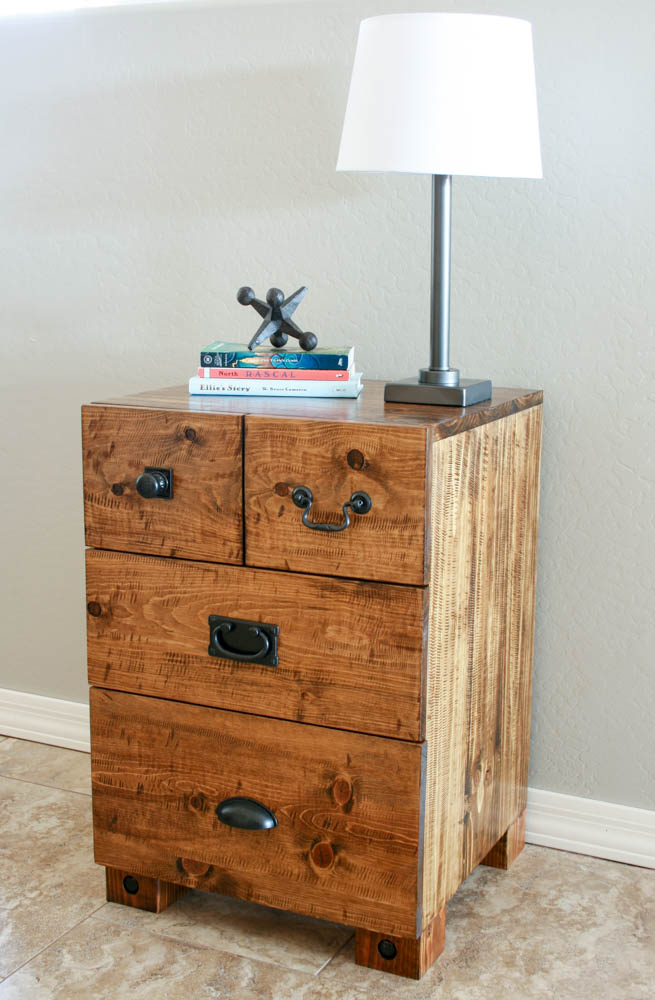 Finished DIY rustic nightstand with three drawers, mixed black hardware, 4x4 legs with decorative lag bolts, styled with books and lamp, stained in Minwax Provincial