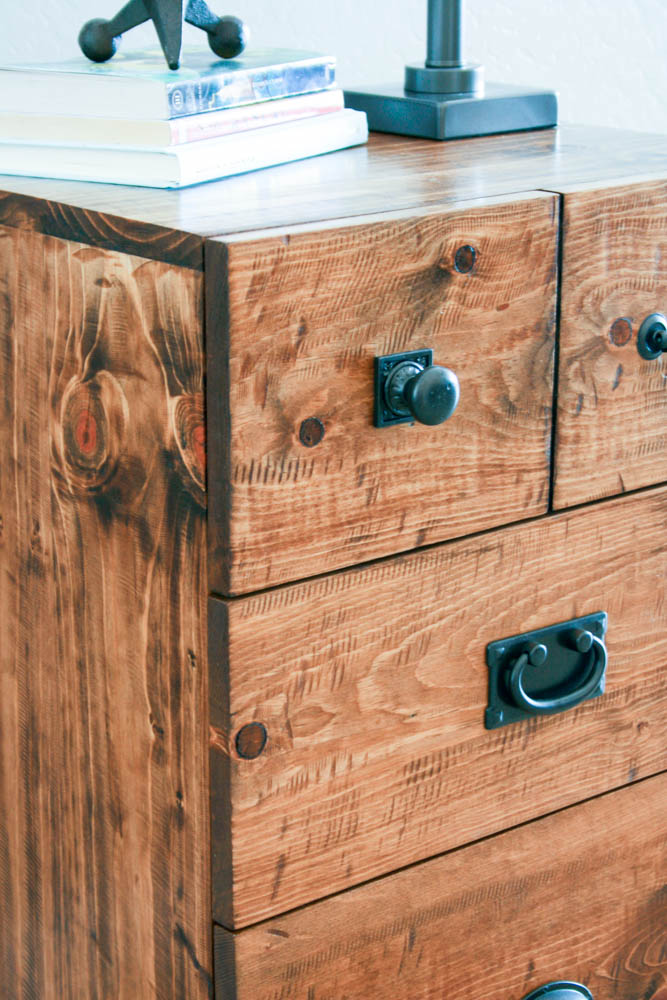 Close-up of distressed pine drawer fronts on DIY nightstand showing grinder saw-mark texture, wood knots, and mixed black cabinet knob and bail pull hardware