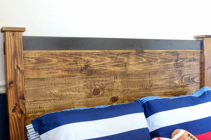 Close-up of DIY rustic headboard showing horizontal wood plank facing and oil rubbed bronze metal roof flashing cap across the top