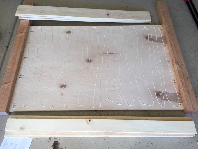 Wood glue applied in wavy lines across plywood headboard backing before attaching 1x4 and 1x6 face boards