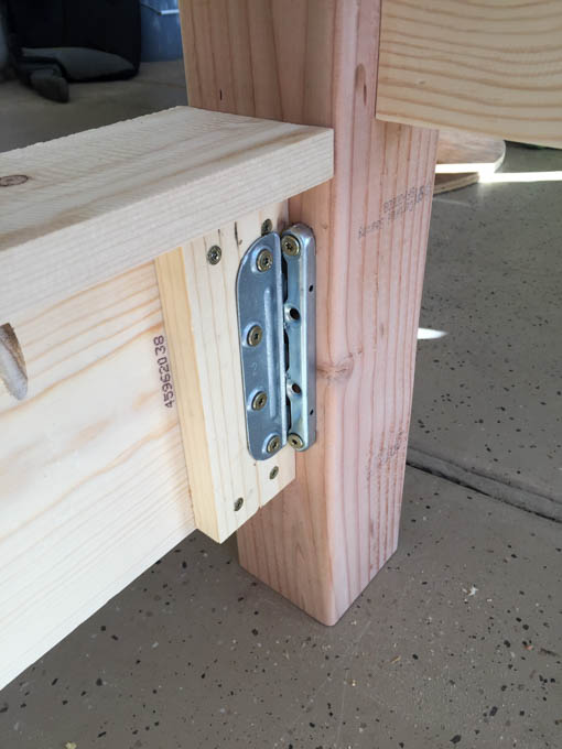 Metal bed rail bracket attached to a 4x4 leg and side rail end showing hardware used for disassemblable bed frame connection