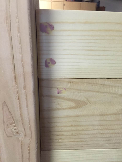 Pink Elmer's color change wood filler visible in nail holes on unstained pine headboard boards, showing filler before it dries white