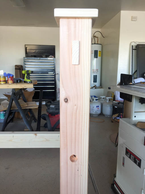 Unfinished 4x4 headboard leg with square post cap on top and drilled lag bolt hole showing decorative detail before staining