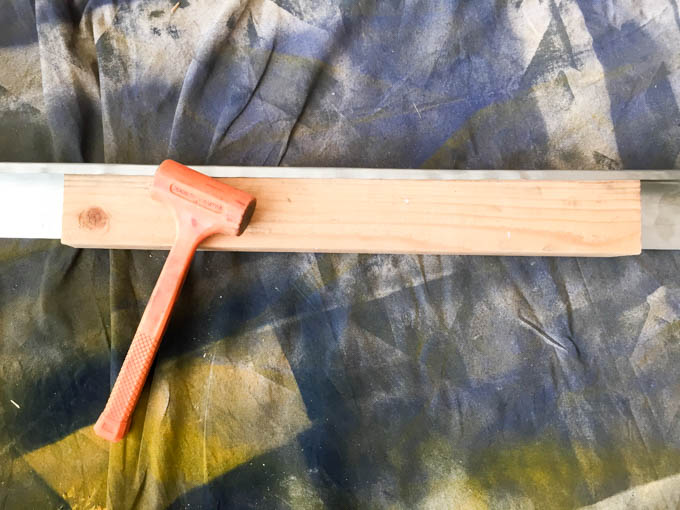 2x3 inch roof flashing strip with a 2x4 used as a bending guide to wrap the metal cap over the top of the DIY headboard