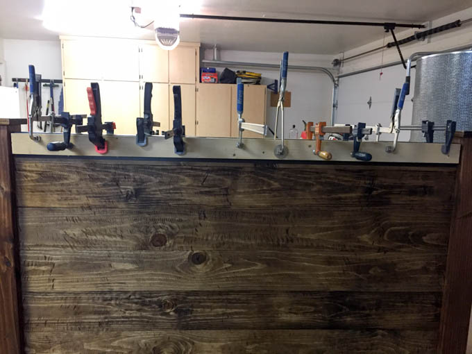 Multiple clamps holding oil rubbed bronze painted roof flashing against the top of a stained wood headboard while glue cures overnight