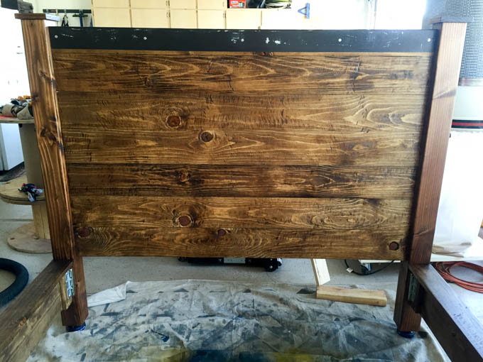 Completed stained rustic headboard with metal cap and post caps on 4x4 legs sitting in the workshop before final assembly