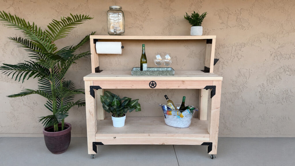 Finished DIY mobile outdoor console table with upper shelf, paper towel holder, and star accent styled with drinks and plants on a patio