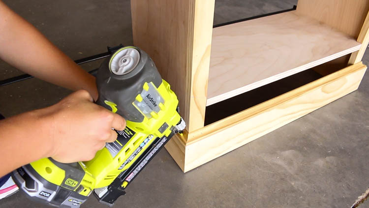 Nailing cove molding into place along the bottom edge of the cabinet