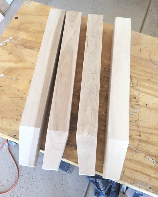 Four unfinished tapered maple furniture legs laid out on a workbench, ready for a DIY narrow hallway table build