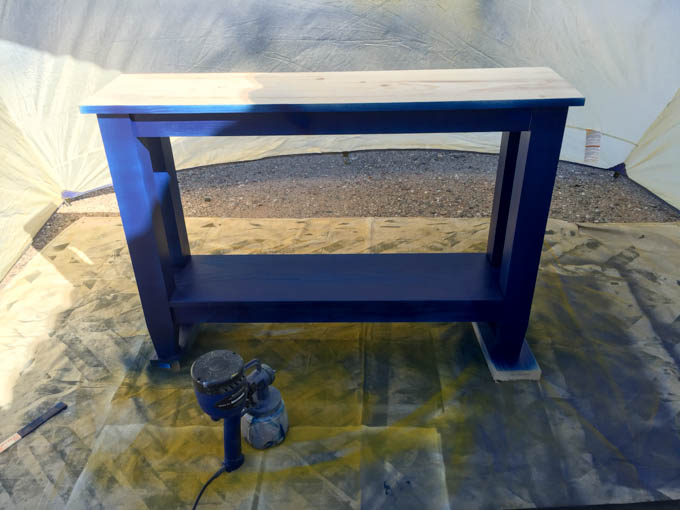 Narrow console table freshly sprayed navy blue with a HomeRight Finish Max sprayer, sitting inside a spray shelter