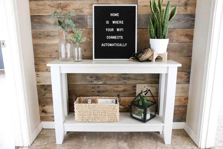 Narrow hallway table repainted gray, styled with a letter board, snake plant, and eucalyptus stems against a pallet wood wall
