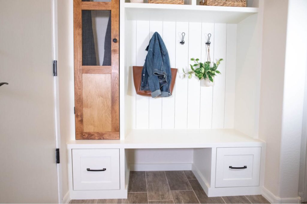 White built-in mudroom bench with two storage drawers, shiplap backing and a tall wood cabinet