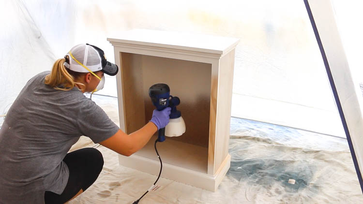Painting the cabinet body Swiss Coffee with a paint sprayer