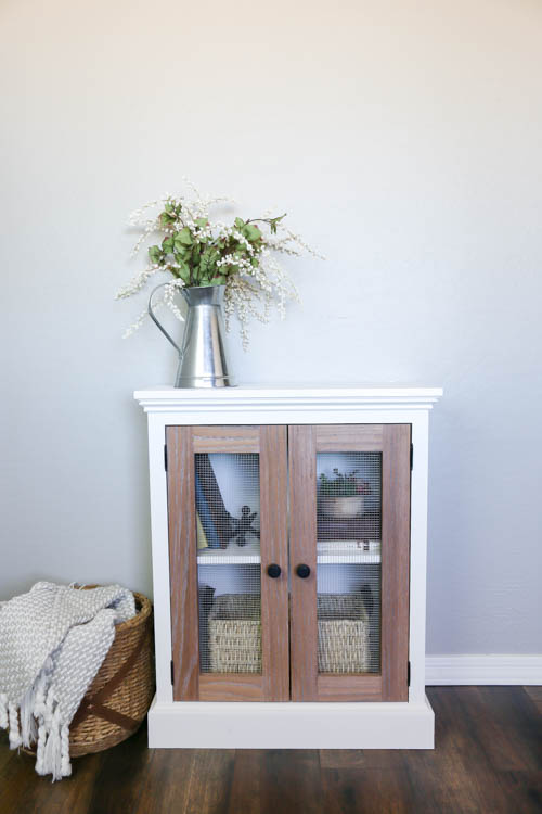 front facing view of the styled two tone cabinet with a vase of flowers on it