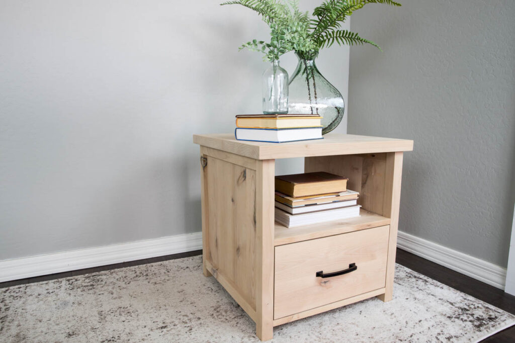 Natural wood DIY side table with storage drawer and open shelf styled in a living room corner with books and a plant