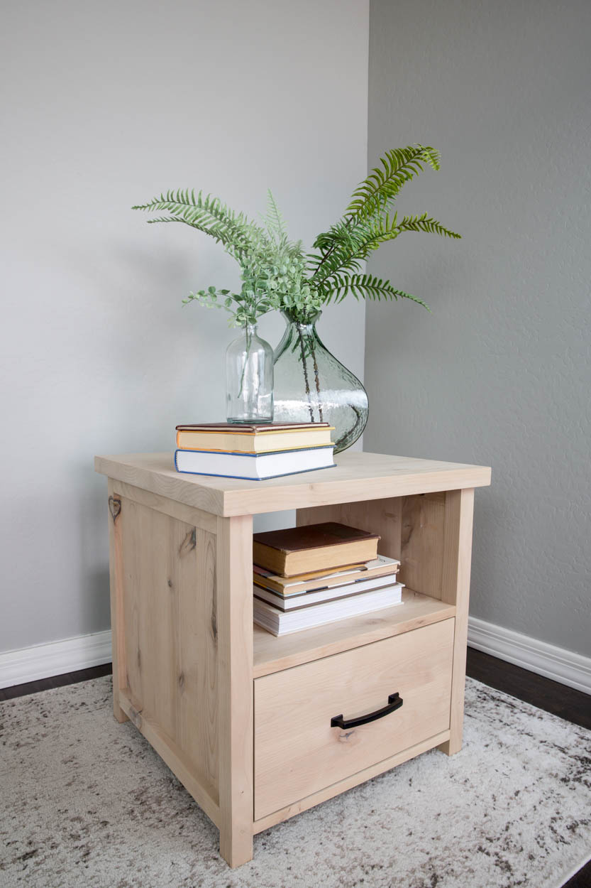 Finished natural wood DIY side table with an open book shelf and closed storage drawer, styled with a plant and stacked books