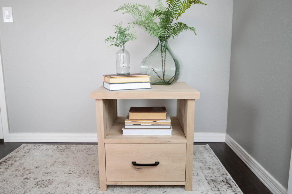 DIY wood side table with a closed drawer and open shelf, styled with stacked books and two glass vases with greenery