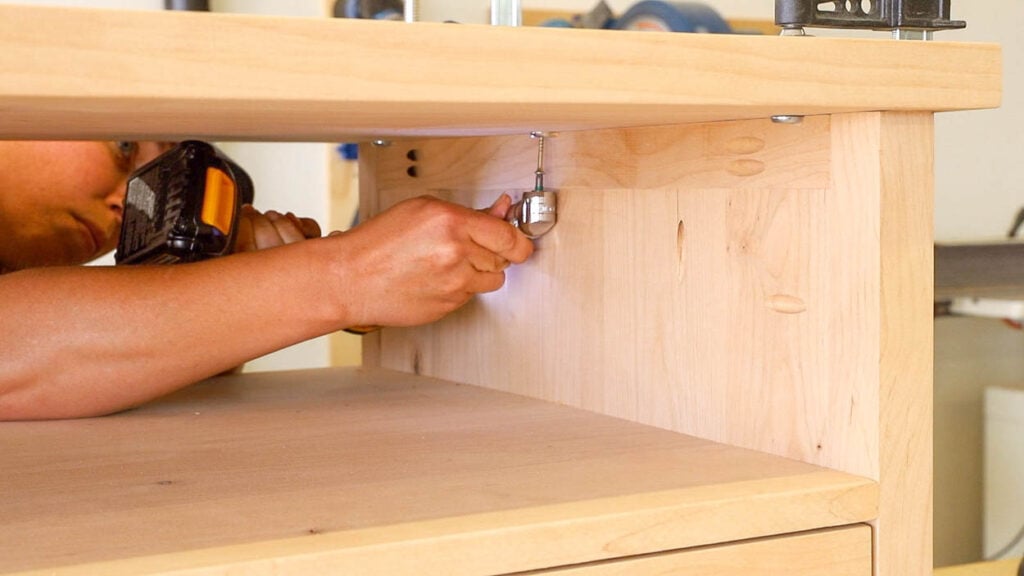 Right-angle drill adapter driving a screw through a desktop fastener into the underside of the tabletop