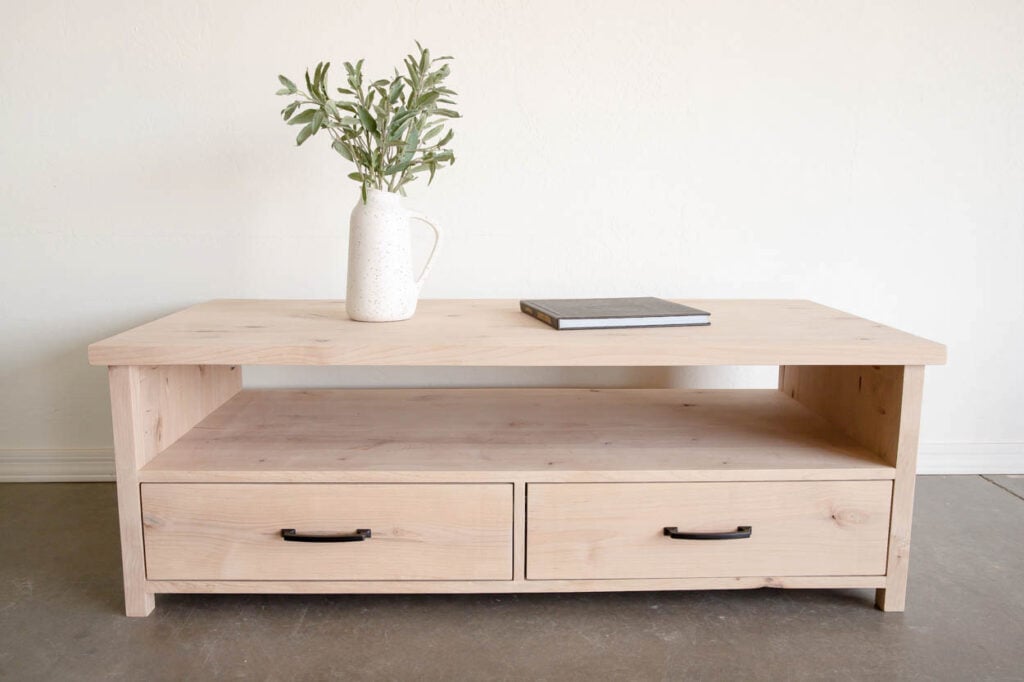 Front view of an unfinished alder coffee table with an open shelf above two equal storage drawers